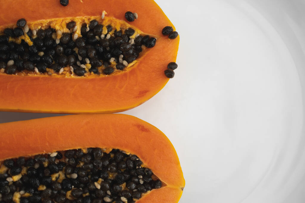 Halfgesneden rijpe papaya met zaad op een wit bord. Snijwonden van zoete papaya met een witte achtergrond. Halve papaja 's. Gezonde exotische vruchten. Vegetarisch voedsel. - Foto, afbeelding