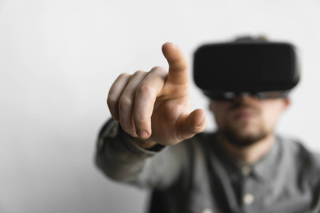 Νέος άνθρωπος με γένια με εικονικά γυαλιά πραγματικότητας που προσπαθούν να αγγίξουν κάτι ή να πατήσουν ένα πράγμα μπροστά σε αυτό που βλέπει. Σύγχρονες τεχνολογίες. Η έννοια της μελλοντικής τεχνολογίας. - Φωτογραφία, εικόνα