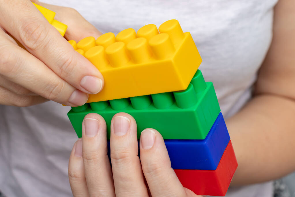 Ruce konstrukce z barevných hraček plastové cihly, bloky pro stavbu na bílém pozadí - Fotografie, Obrázek