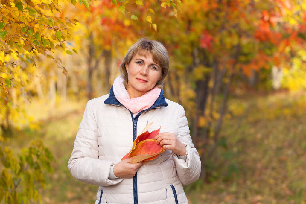Μια μεσήλικη γυναίκα περπατά το φθινόπωρο στο πάρκο ανάμεσα στα δέντρα.. - Φωτογραφία, εικόνα