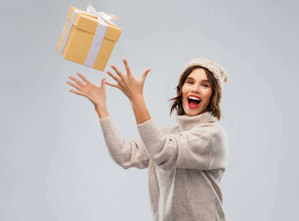 νεαρή γυναίκα σε χειμερινό καπέλο αλίευση κουτί δώρου - Φωτογραφία, εικόνα
