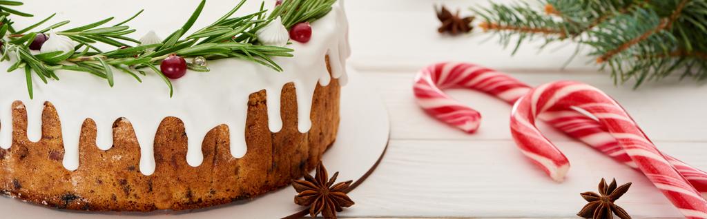 γλυκιά χριστουγεννιάτικη πίτα με κερασάκι σε λευκό ξύλινο τραπέζι με καραμέλες και κλαδιά ερυθρελάτης - Φωτογραφία, εικόνα