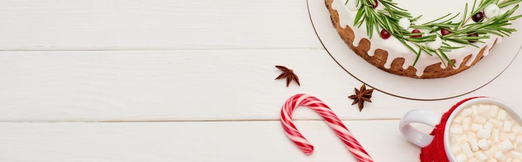 κορυφαία άποψη της χριστουγεννιάτικης πίτας σε λευκό ξύλινο τραπέζι με ζαχαροκάλαμο καραμέλα και φλιτζάνι κακάο με marshmallows - Φωτογραφία, εικόνα