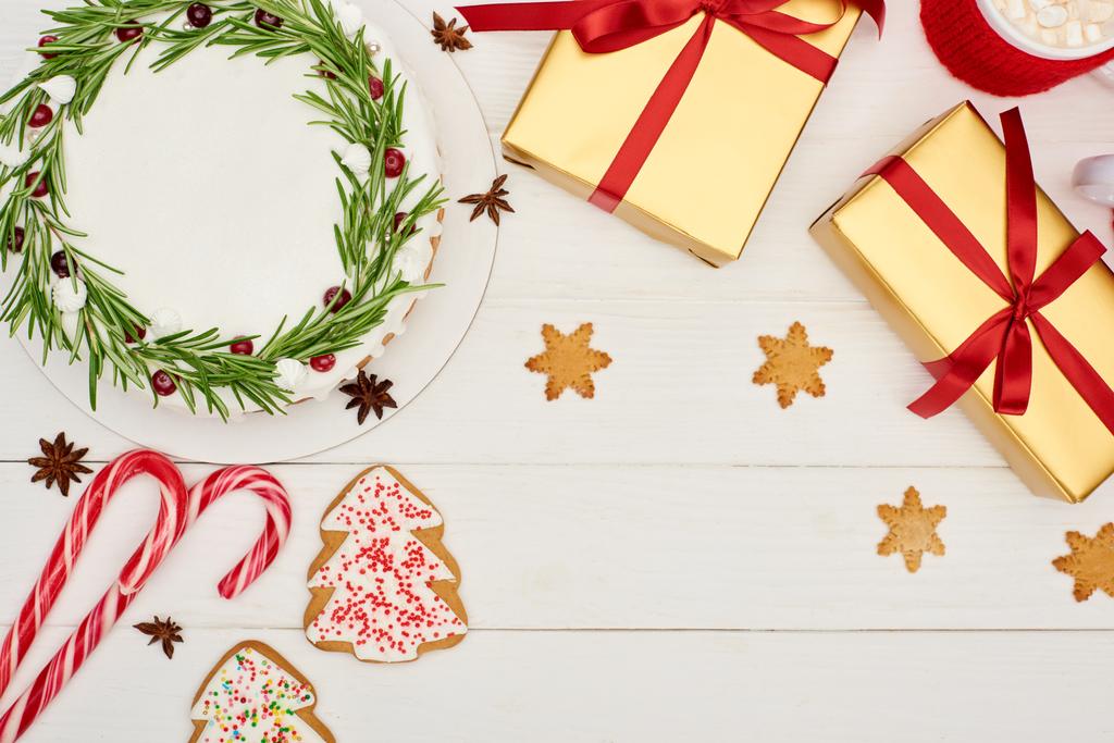 vrchní pohled na vánoční koláč, sušenky a dárky na bílém dřevěném stole - Fotografie, Obrázek