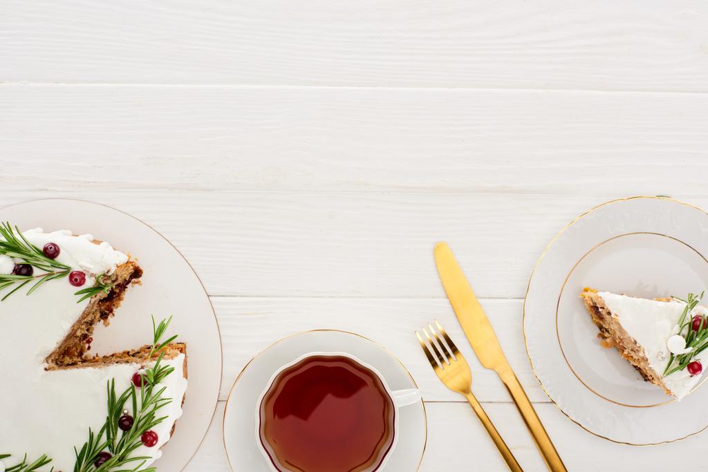 bovenaanzicht van kersttaart met rozemarijn en kopje thee op witte houten tafel - Foto, afbeelding