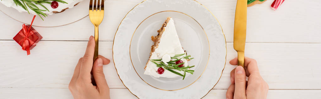 oříznutý pohled na dívku drží vidličku a nůž jíst vánoční koláč a sušenky na bílém dřevěném stole - Fotografie, Obrázek