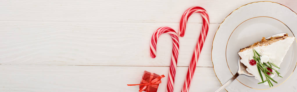 vista superior del pedazo de pastel de Navidad con romero y arándanos sobre una mesa de madera blanca con bastones de caramelo y pequeño regalo
 - Foto, imagen