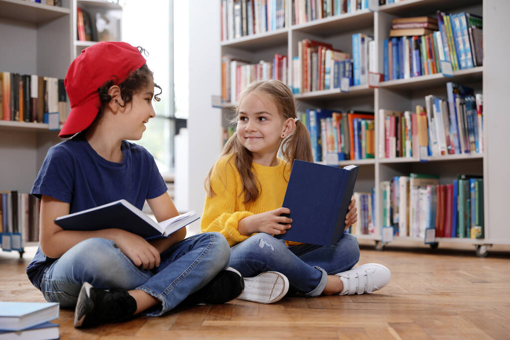 Kütüphanede yerde kitap okuyan şirin küçük çocuklar. - Fotoğraf, Görsel