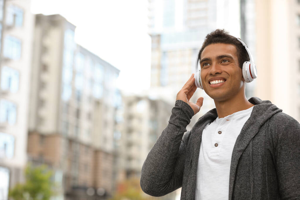 Retrato de un joven afroamericano guapo con auriculares escuchando música en la calle de la ciudad. Espacio para texto
 - Foto, Imagen