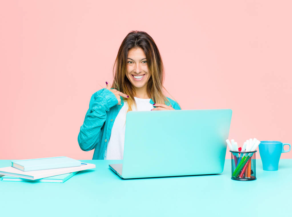 jovem mulher bonita trabalhando com um laptop olhando feliz, orgulhoso e surpreso, alegremente apontando para si mesmo, sentindo-se confiante e alto
 - Foto, Imagem