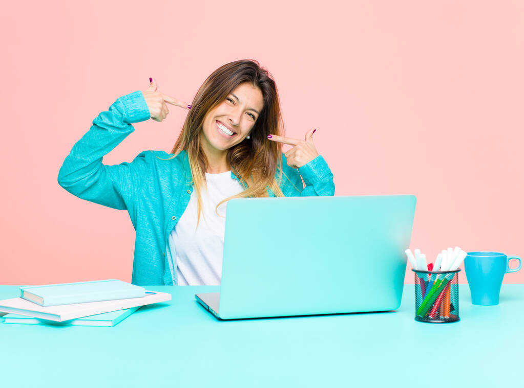 nuori kaunis nainen työskentelee kannettavan tietokoneen hymyillen luottavaisesti osoittaa omaa leveä hymy, positiivinen, rento, tyytyväinen asenne
 - Valokuva, kuva