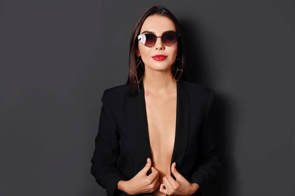Beautiful woman wearing jacket and sunglasses on black background - Photo, Image