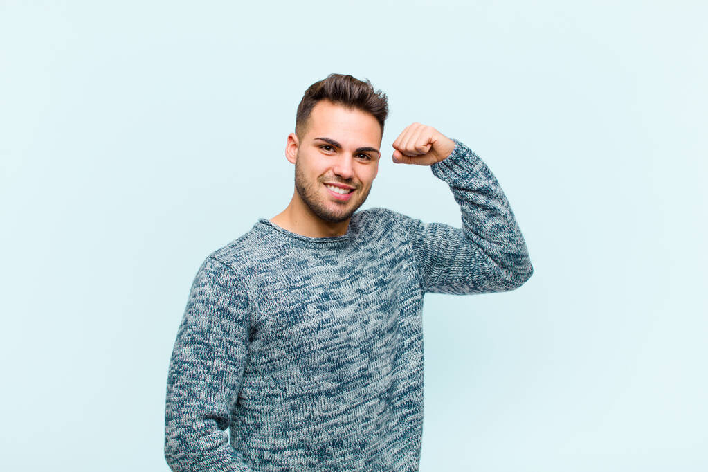 joven hombre hispano sintiéndose feliz, satisfecho y poderoso, ajuste flexible y bíceps musculosos, mirando fuerte después del gimnasio sobre fondo azul
 - Foto, imagen
