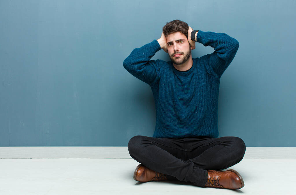 mladý pohledný muž sedící na podlaze s pocitem stresu, obav, úzkosti nebo strachu, s rukama za hlavou, zmateně panikaří - Fotografie, Obrázek