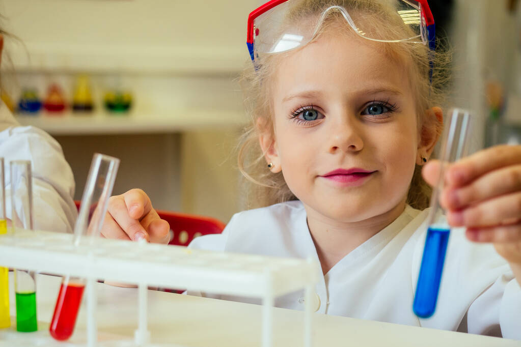 okos szőke iskolás lány vegyész szemüveg és fehér orvosi köpeny, hogy tudományos kísérletek kémia, keverés különböző kémiai megoldások laboratóriumi osztályteremben - Fotó, kép