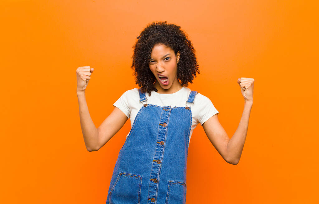 jovem bonita mulher negra sentindo-se feliz, surpreso e orgulhoso, gritando e celebrando o sucesso com um grande sorriso contra a parede laranja
 - Foto, Imagem