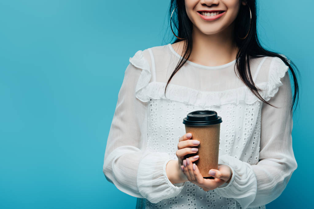 recortado vista de sonriente morena asiática mujer sosteniendo café para ir sobre fondo azul
 - Foto, imagen