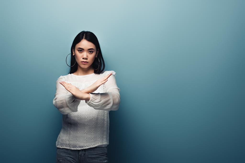 upset brunette asian woman showing stop gesture on blue background - Photo, Image