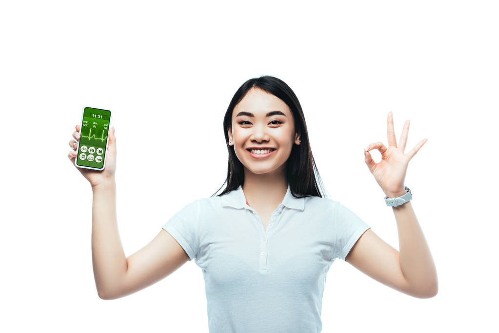felice bruna donna asiatica in possesso di smartphone con app sanitaria e mostrando segno ok isolato su bianco
 - Foto, immagini
