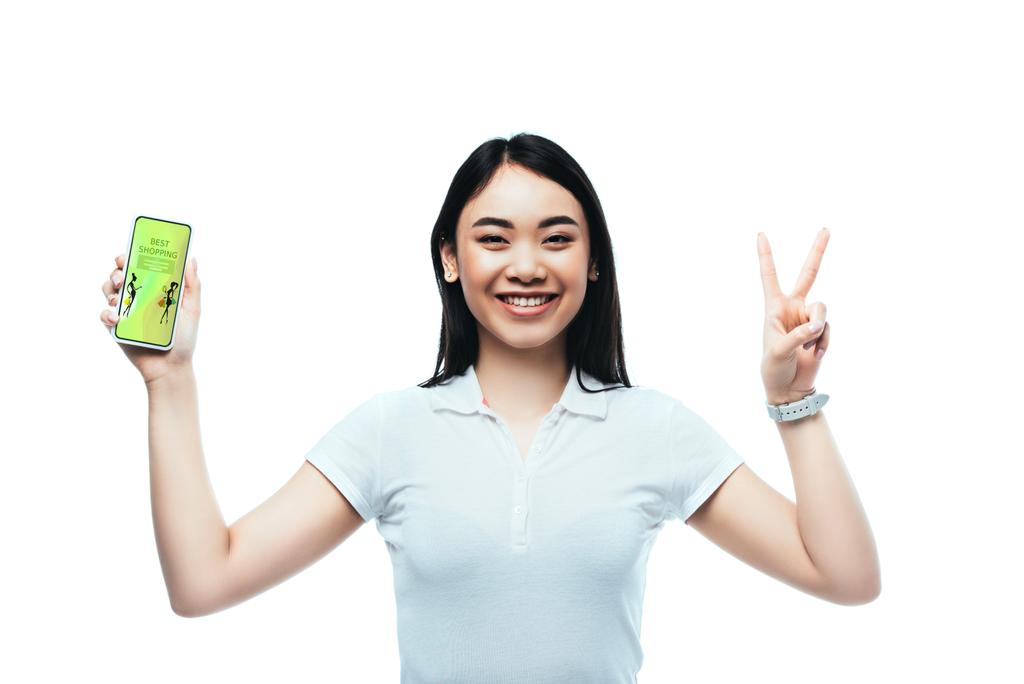 morena feliz mujer asiática sosteniendo teléfono inteligente con la mejor aplicación de compras y mostrando signo de paz aislado en blanco
 - Foto, Imagen