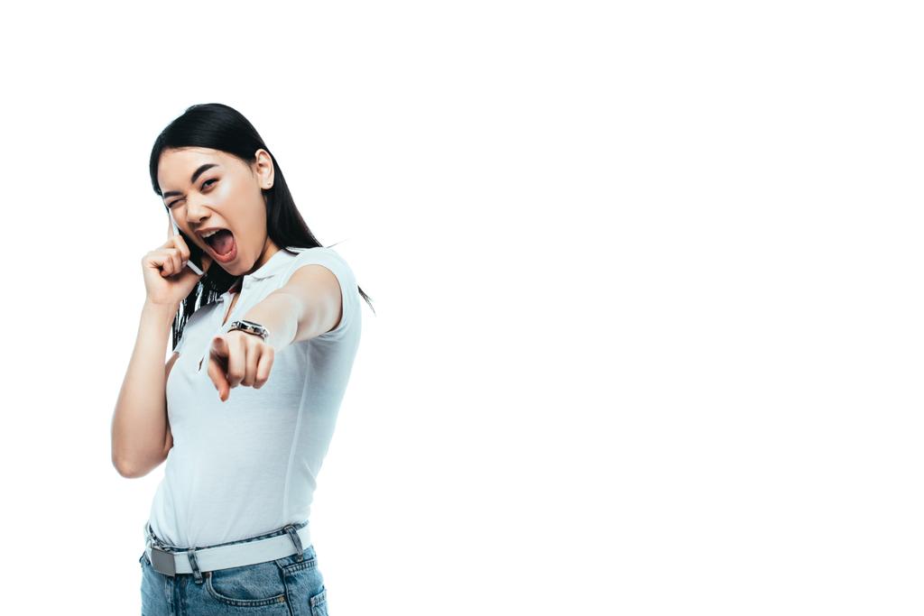 возбужденный брюнетка азиатская женщина говорит на смартфоне и указывая пальцем на камеру изолированы на белом
 - Фото, изображение