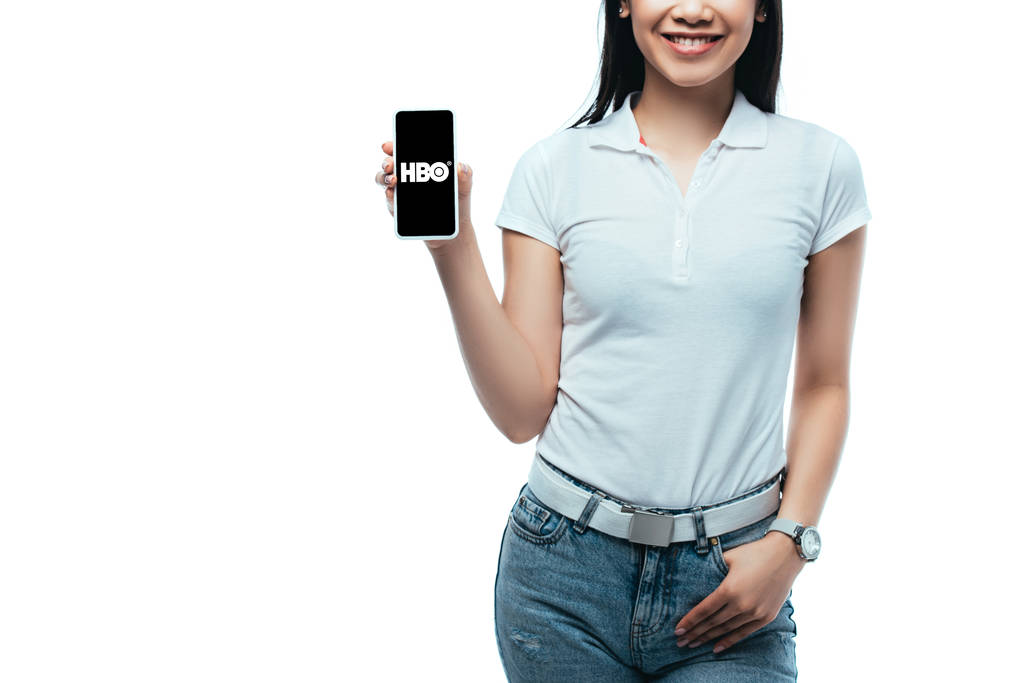 KYIV, UKRAINE - JULY 15, 2019: cropped view of smiling brunette asian woman holding smartphone with HBO app isolated on white - Photo, Image