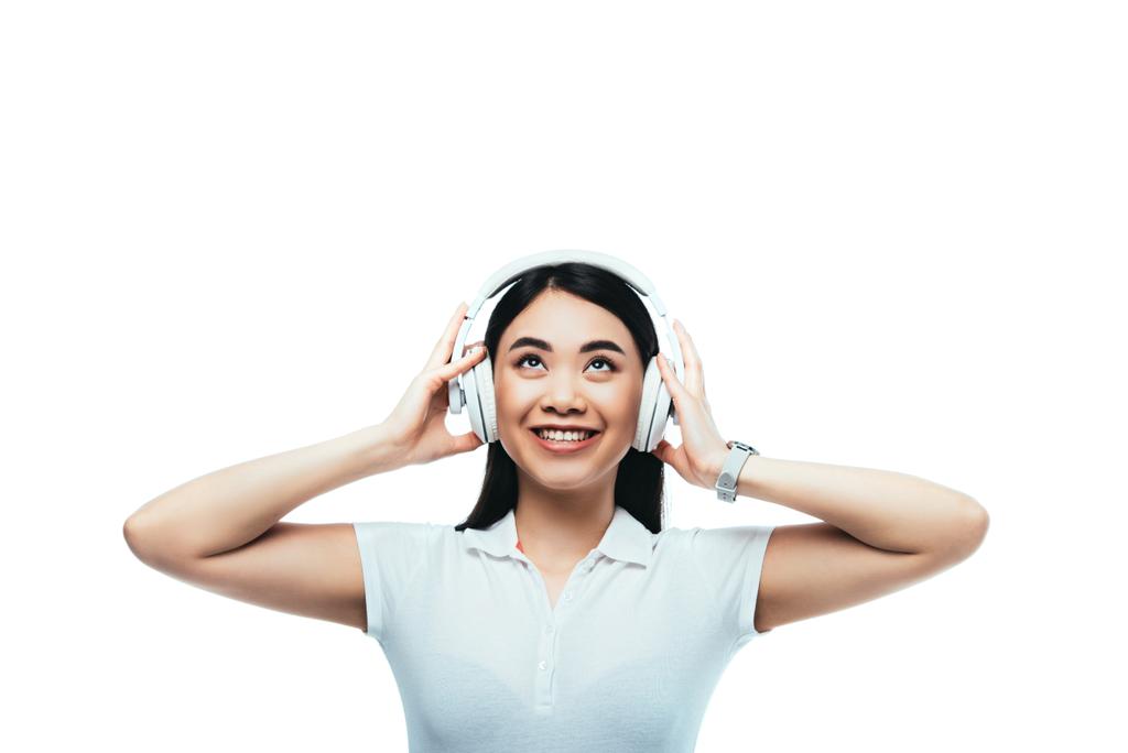 χαμογελαστή ελκυστική Ασιάτισσα με ακουστικά που κοιτάζει απομονωμένη στα λευκά - Φωτογραφία, εικόνα