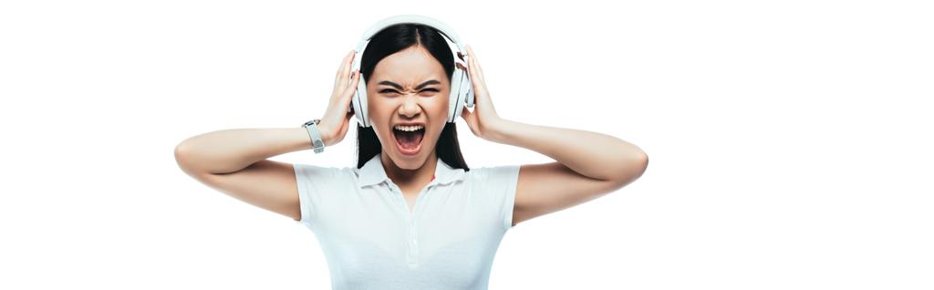 zły atrakcyjny Azji dziewczyna krzyczy w słuchawki izolowane na biały, panoramiczny strzał - Zdjęcie, obraz