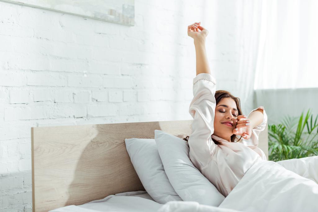 aantrekkelijke vrouw met gesloten ogen stretching zichzelf in de ochtend  - Foto, afbeelding