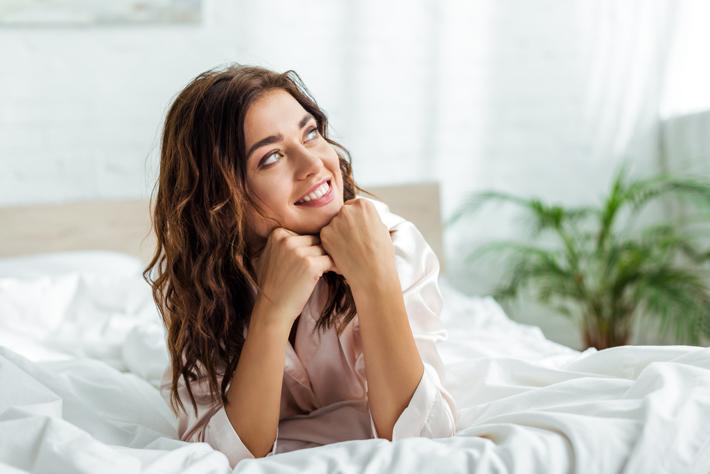 glimlachende vrouw liggend in bed en kijken weg in de ochtend  - Foto, afbeelding