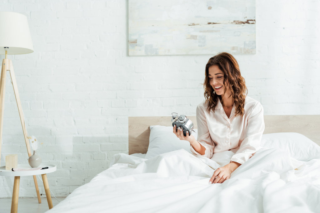 attraente donna sorridente e tenendo sveglia al mattino
  - Foto, immagini