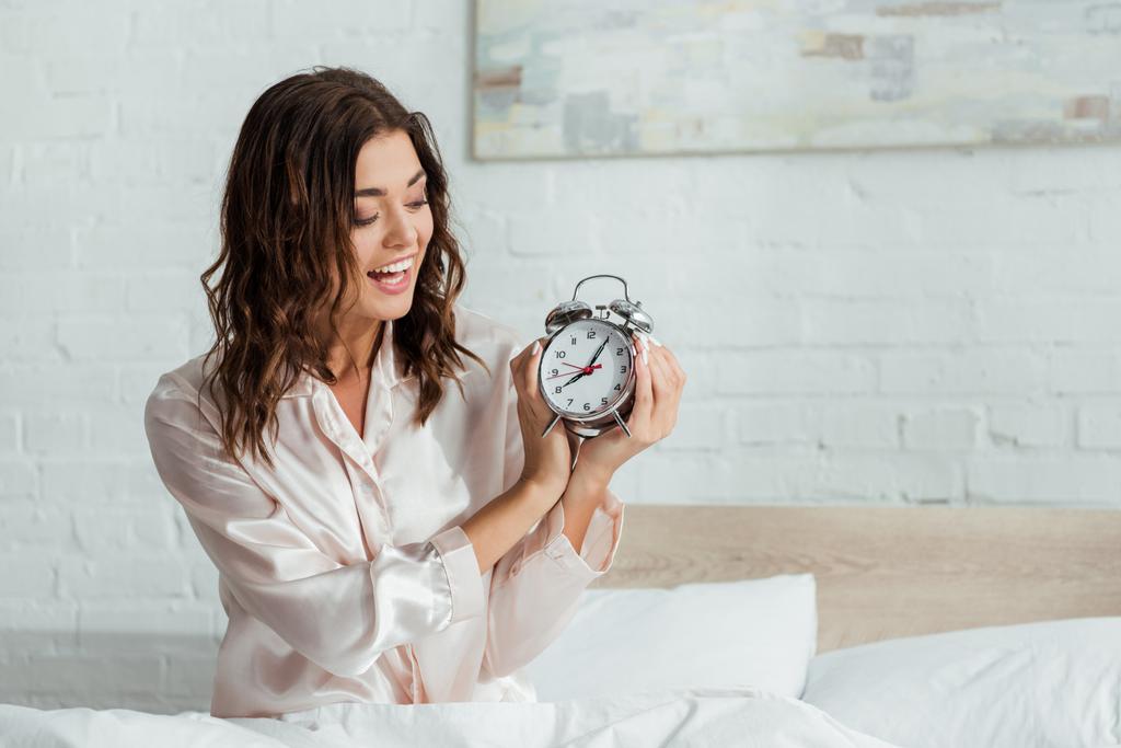 приваблива жінка посміхається і тримає будильник вранці
  - Фото, зображення
