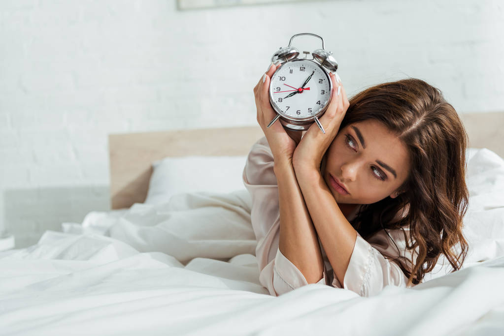 Attractive woman taken 5-HTP holding alarm clock after restful sleep lying in bed at morning