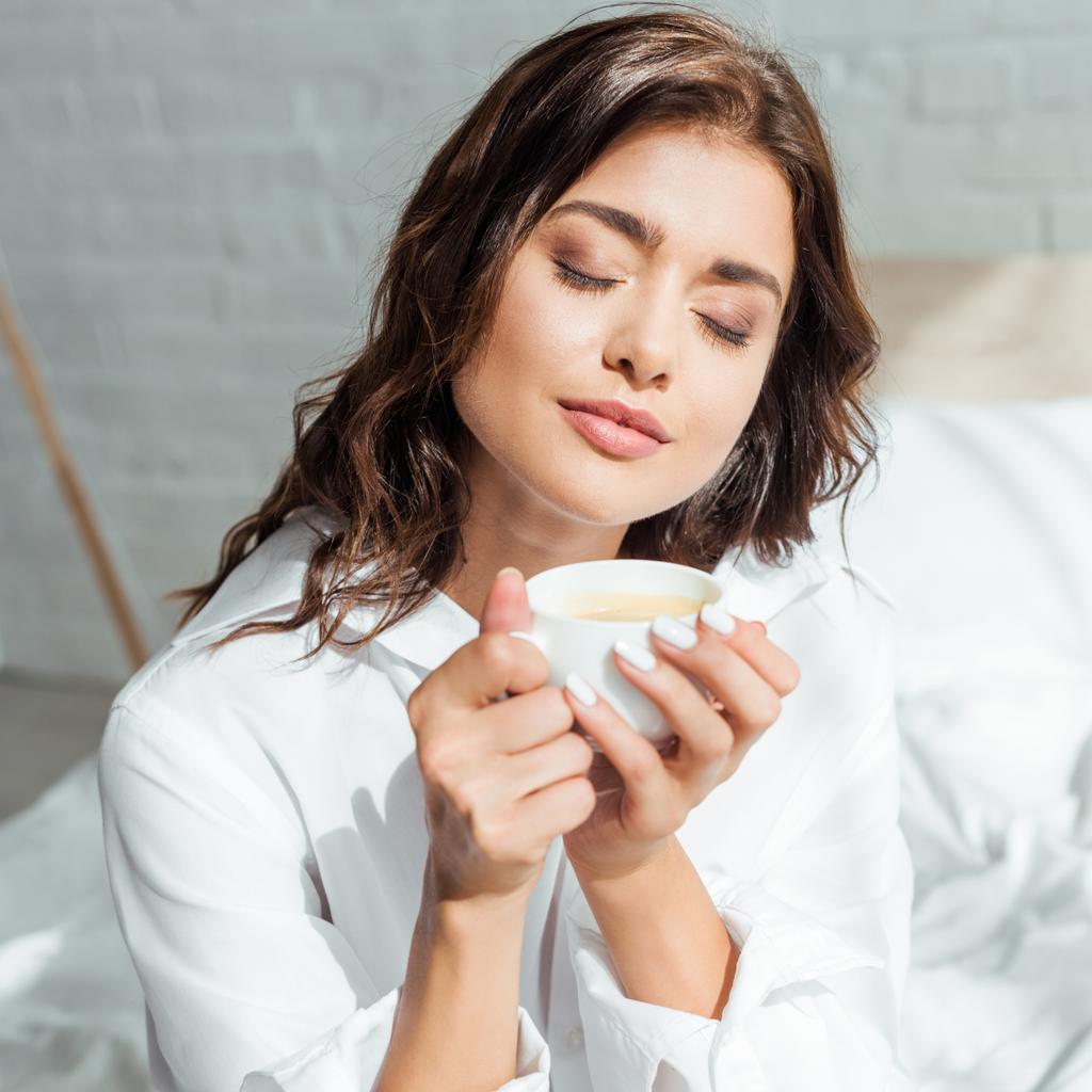 attractive woman in white shirt with closed eyes holding cup at morning  - Photo, Image
