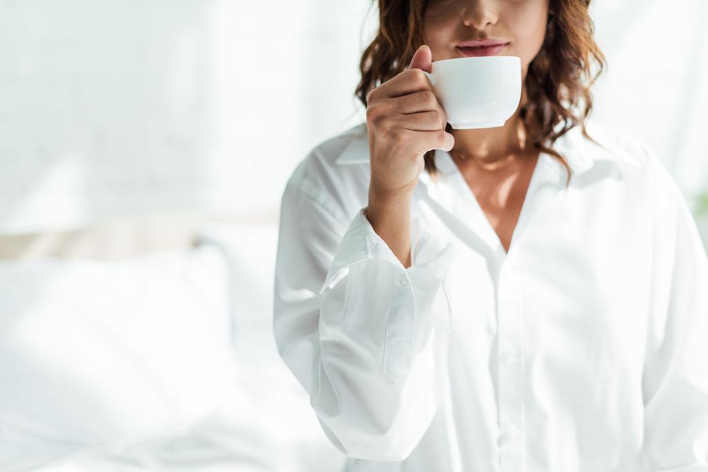 oříznutý pohled na ženu v bílé košili drží pohár v dopoledních hodinách  - Fotografie, Obrázek