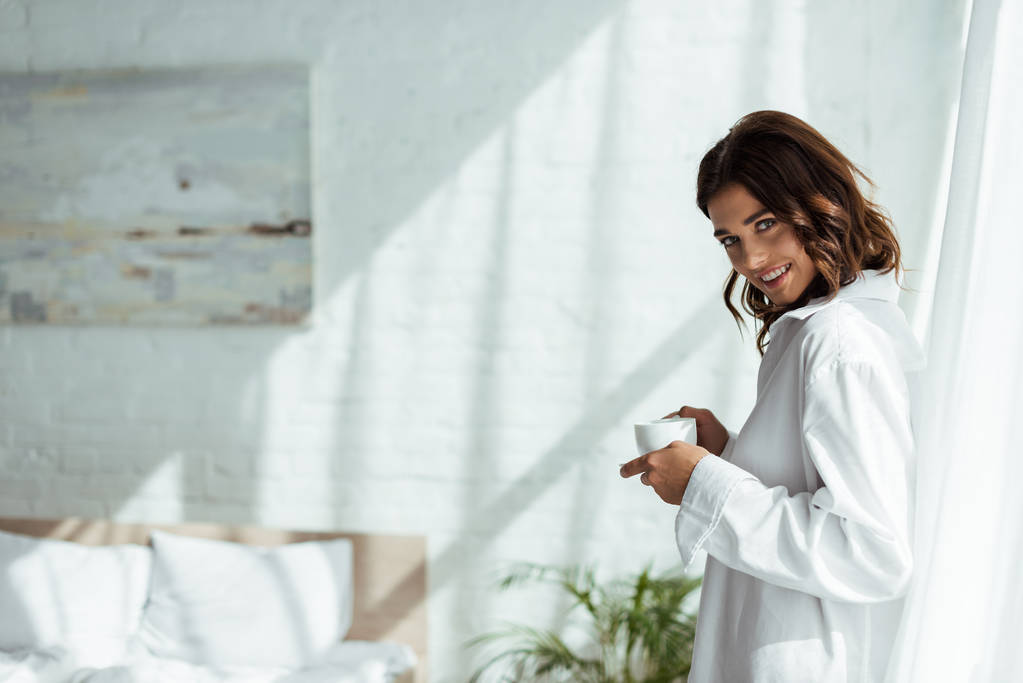 vonzó nő fehér ingben mosolyog és tartja csésze reggel  - Fotó, kép