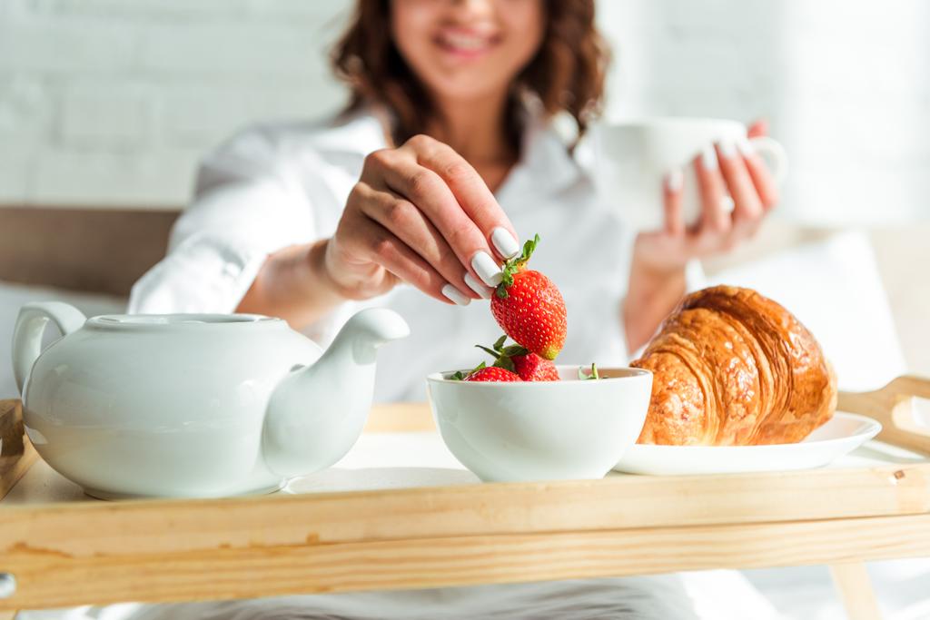 abgeschnittene Ansicht einer Frau, die morgens im Bett frühstückt  - Foto, Bild