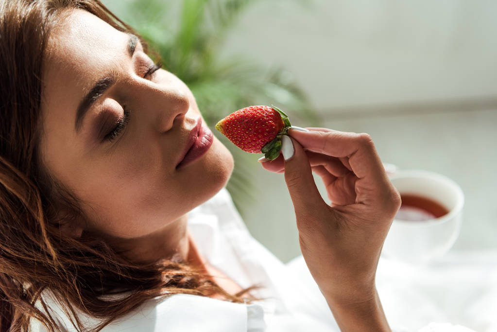 attractive woman with closed eyes holding strawberry at morning  - Photo, Image