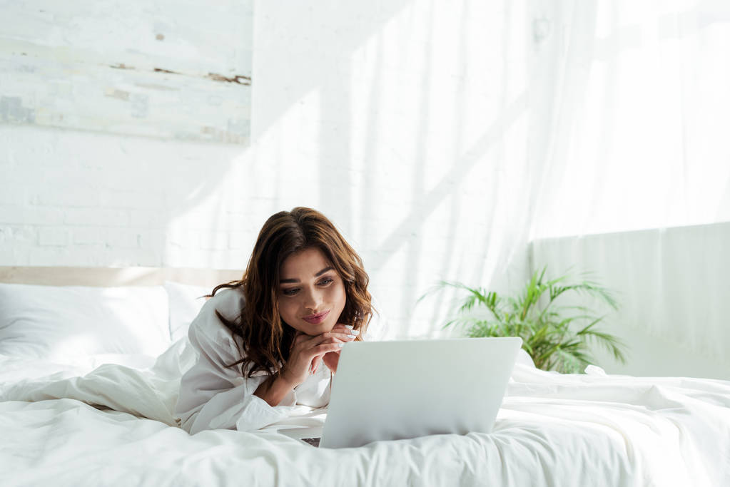 mujer sonriente en camisa mirando el ordenador portátil por la mañana
  - Foto, Imagen