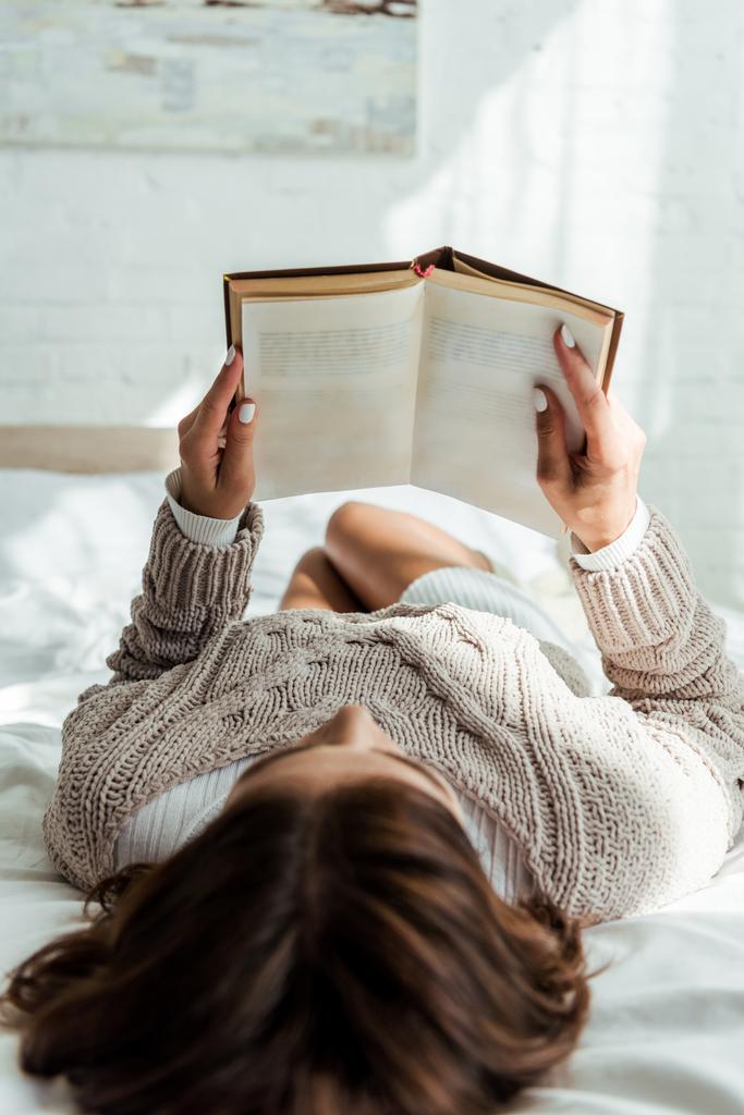 επιλεκτική εστίαση της γυναίκας σε γκρι πουλόβερ βιβλίο ανάγνωσης το πρωί  - Φωτογραφία, εικόνα