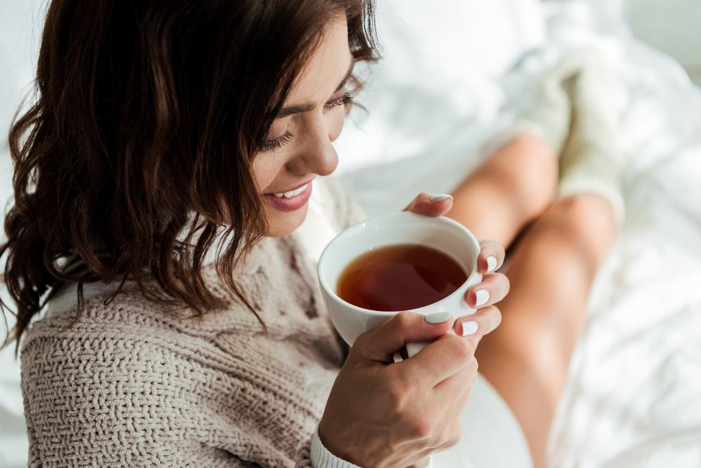 ελκυστική γυναίκα σε γκρι πουλόβερ κρατώντας φλιτζάνι τσάι το πρωί  - Φωτογραφία, εικόνα