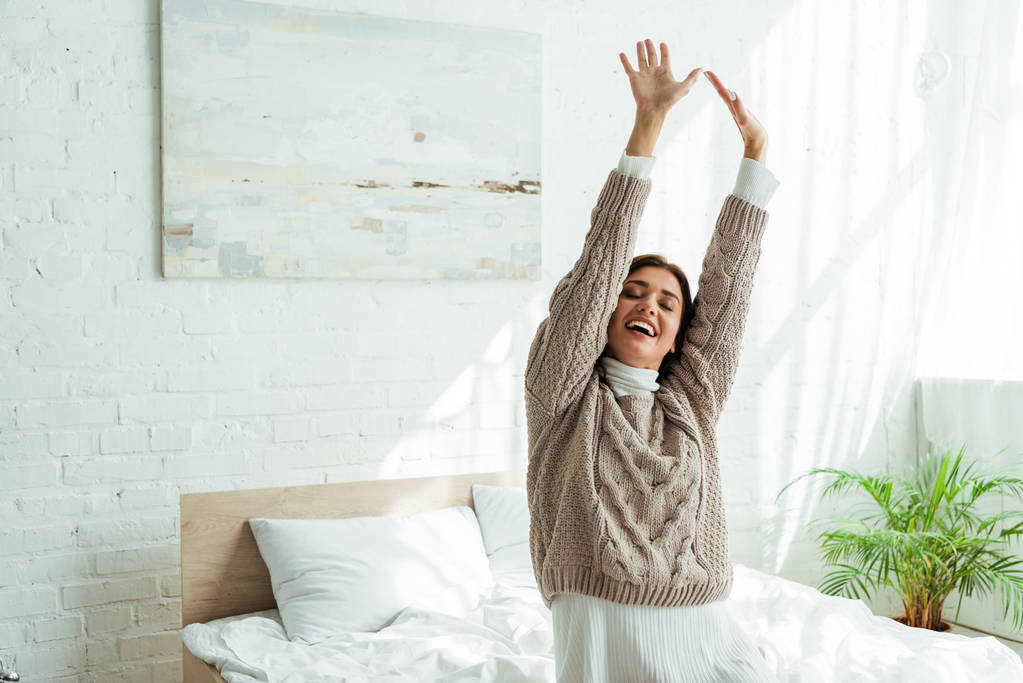 aantrekkelijke en lachende vrouw in trui met uitgestrekte handen in de ochtend  - Foto, afbeelding