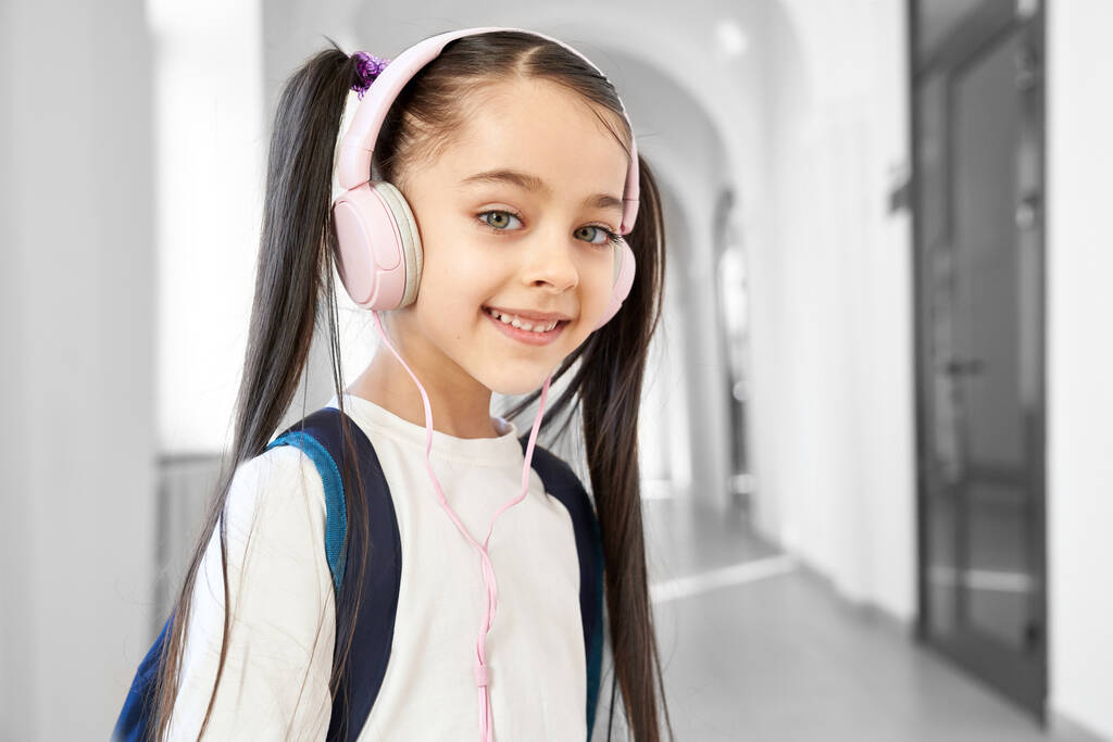 hübsche Schulmädchen mit Kopfhörern posiert im Flur. - Foto, Bild