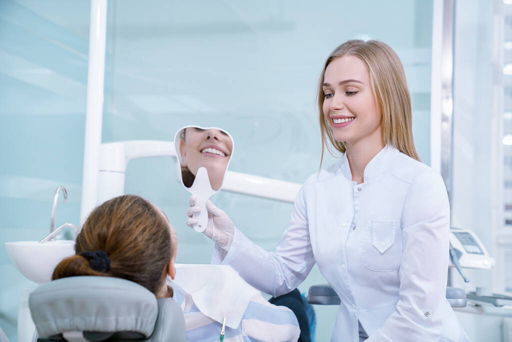 Dentista sosteniendo diente en forma de espejo para el cliente
. - Foto, imagen