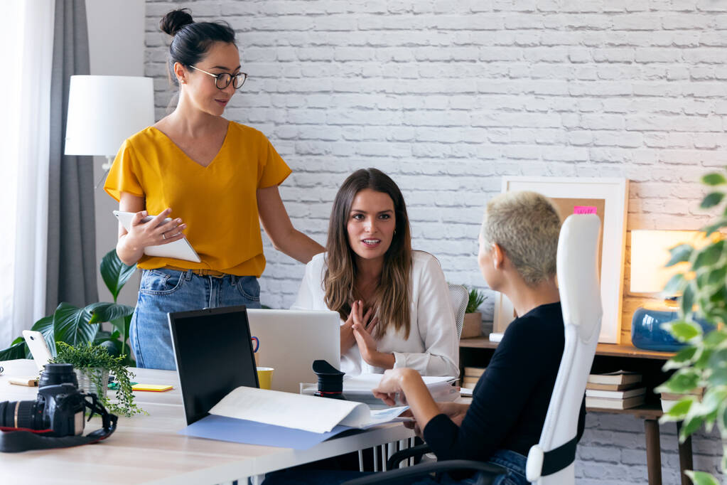 Trzy nowoczesne kobiety przedsiębiorcy, którzy mówią o nowych pomysłach na kolejną pracę we wspólnej przestrzeni roboczej. - Zdjęcie, obraz