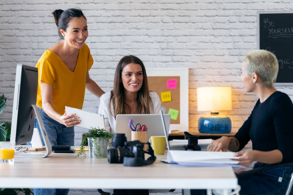 Drie moderne zakenvrouwen praten en evalueren het laatste werk op de computer in een gezamenlijke werkruimte - Foto, afbeelding
