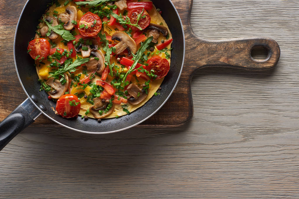 vrchní pohled na domácí omeletu v pánvi na dřevěné desce  - Fotografie, Obrázek