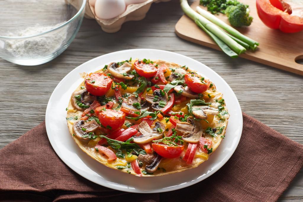 omelete caseiro com legumes na mesa de madeira com guardanapo e ingredientes
 - Foto, Imagem