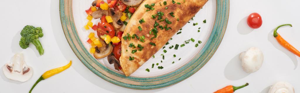 bovenaanzicht van bord met lekker gewikkelde omelet met groenten op witte tafel met ingrediënten  - Foto, afbeelding