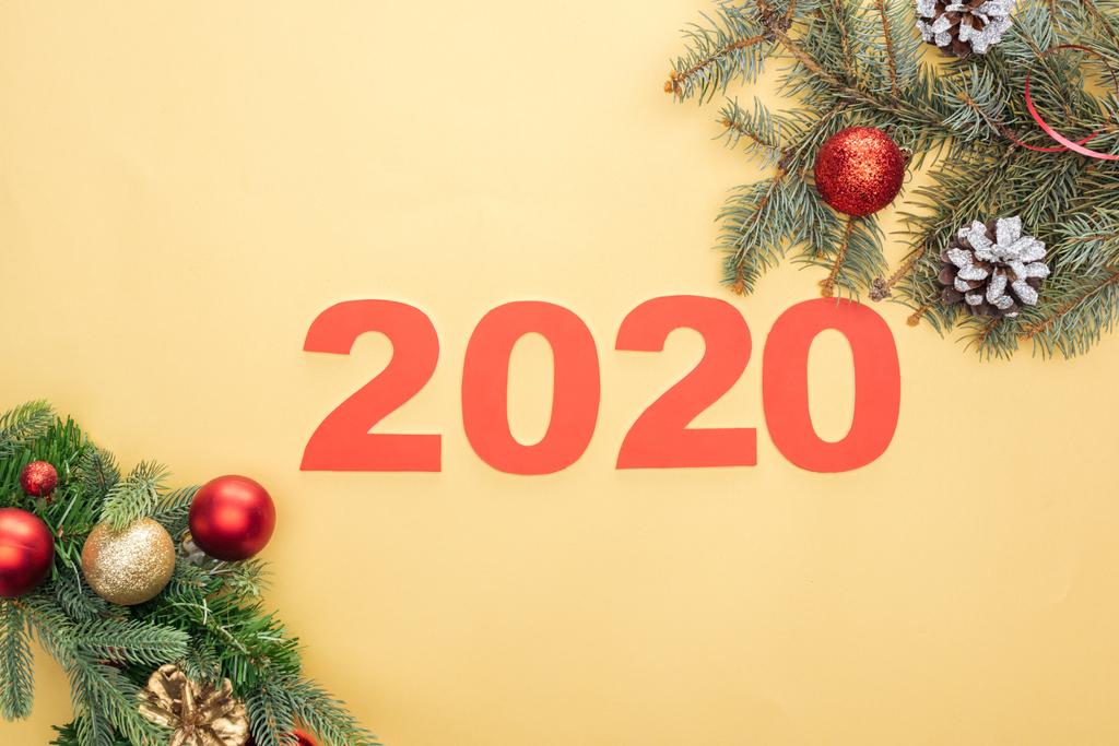 vista superior de los números de papel 2020 cerca de las ramas del árbol de Navidad con adornos y conos sobre fondo amarillo
 - Foto, imagen